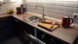 A modern kitchen with a double sink, a coffee maker, a cutting board with a knife, and a loaf of bread.