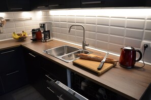 Una cocina moderna con un lavamanos doble, una cafetera, una tabla de cortar con un cuchillo y una hogaza de pan.