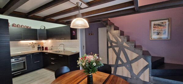 A modern kitchen with dark cabinetry, a built-in oven, and a wooden dining table with a vase of flowers.