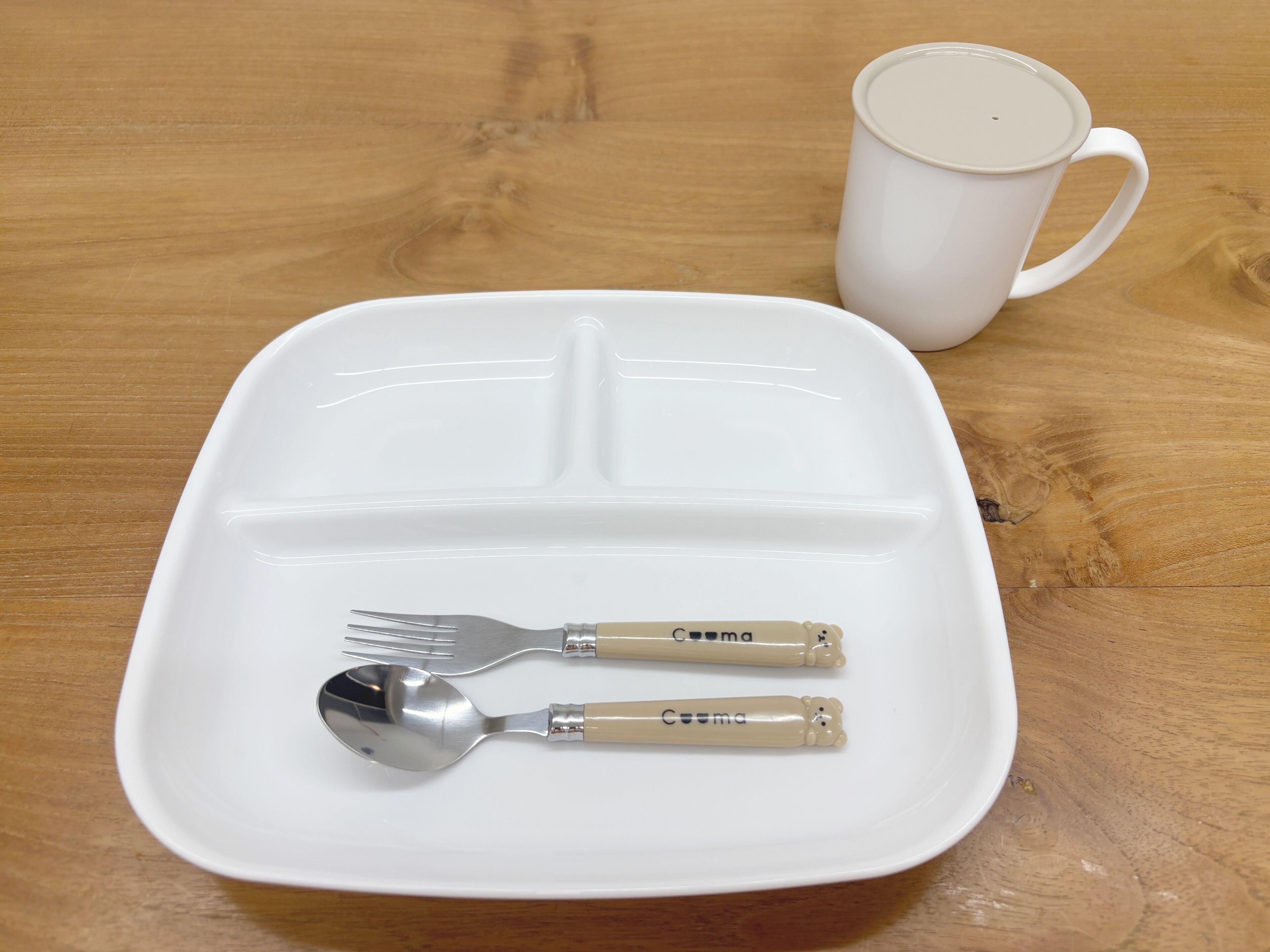 A white plate with a spoon and fork on a wooden table.