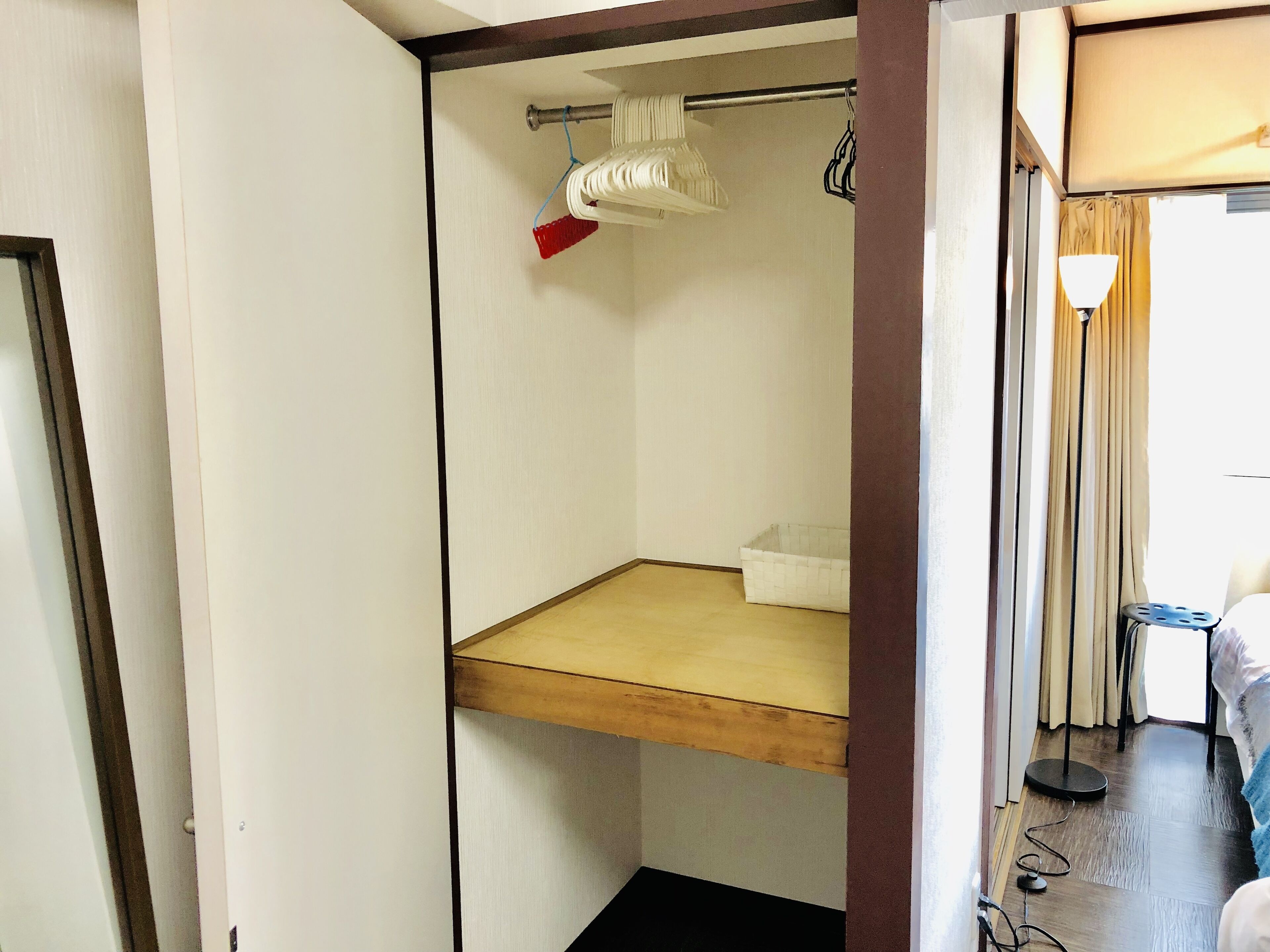 A small, narrow room with a wooden shelf, a white basin, and a red broom.