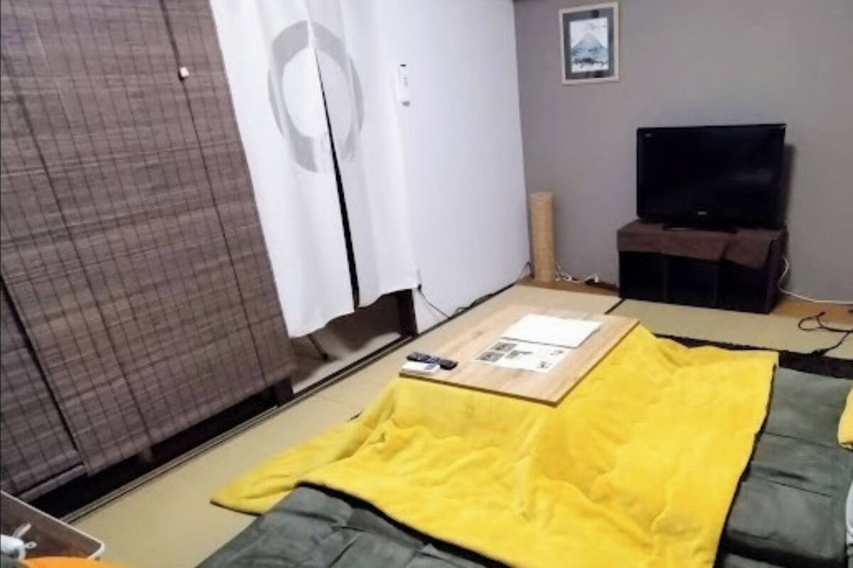 A small, sparsely furnished room with a sliding door, a television, and a futon bed.
