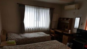 Ett hotellrum med två sängar, ett skrivbord, en stol, en TV och ett fönster med gardiner.