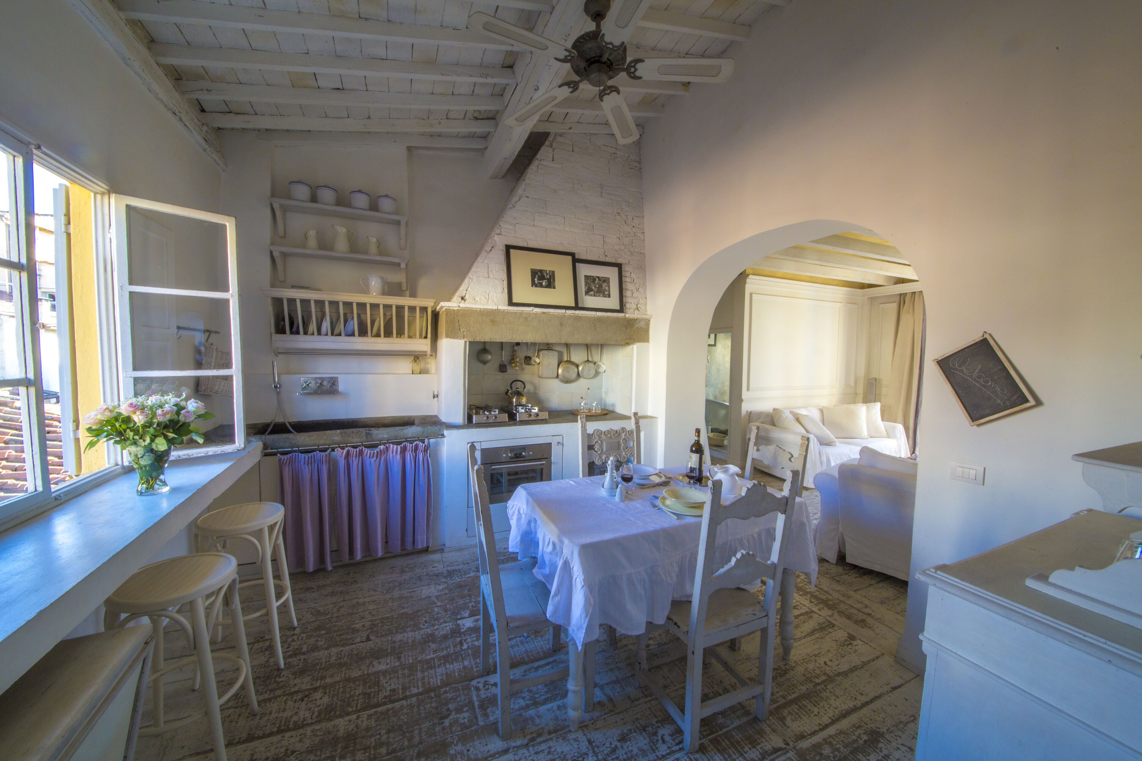 A rustic kitchen with white cabinetry, a dining table set for two, and a window with a view of the outside.