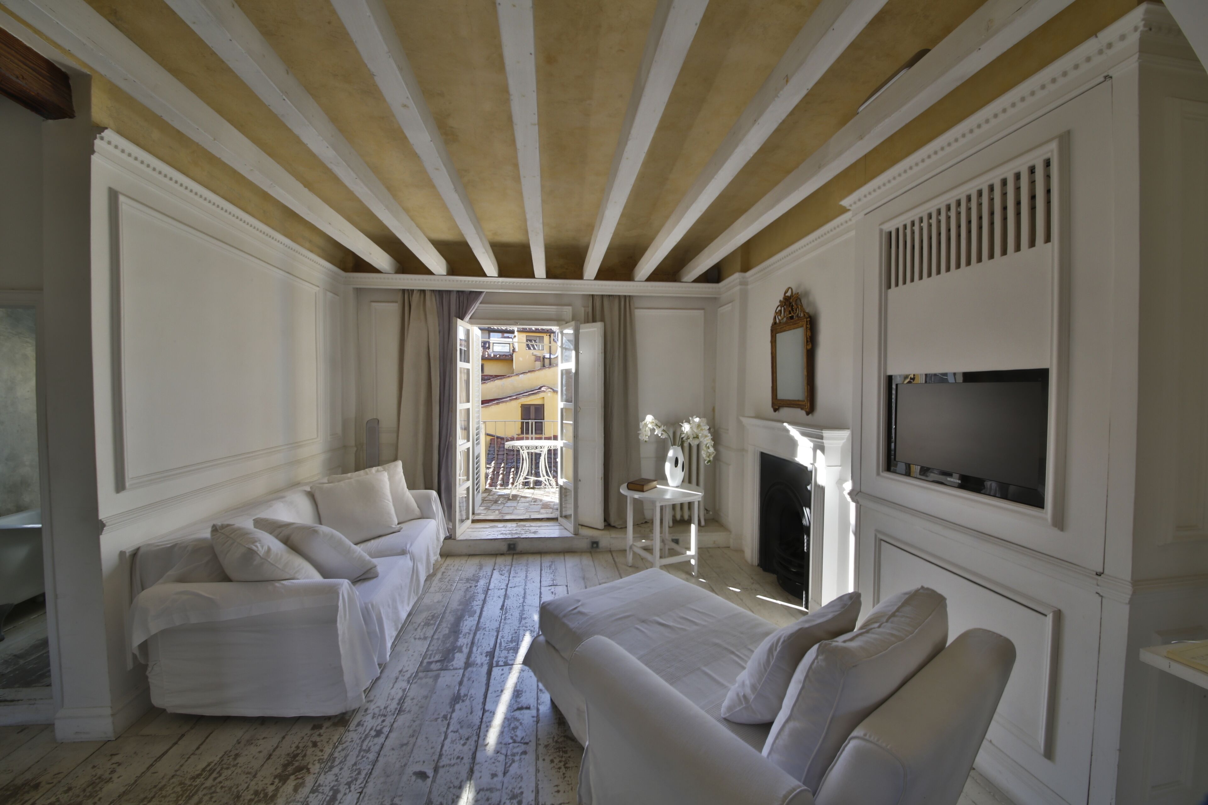 A room with a white sofa, a white armchair, a fireplace, and a television.