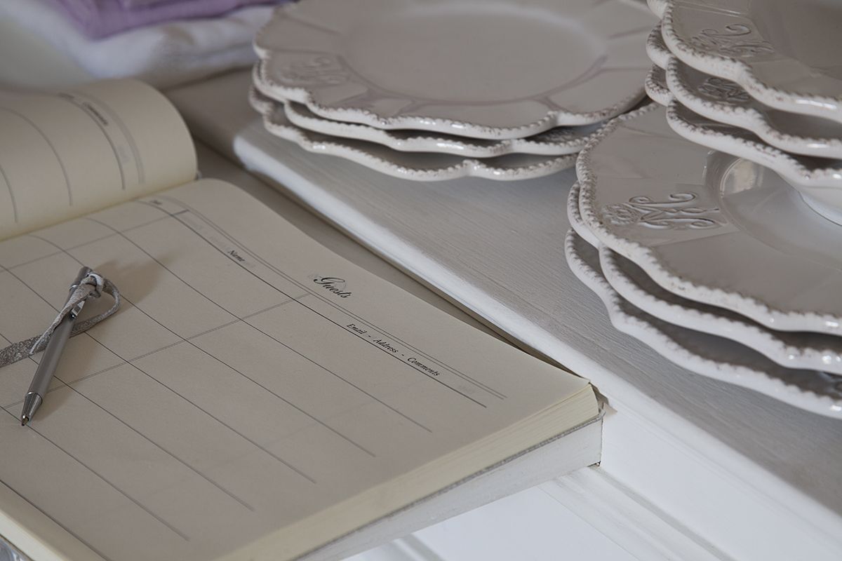 A notebook with a pen on it, next to a stack of white plates with decorative edges.