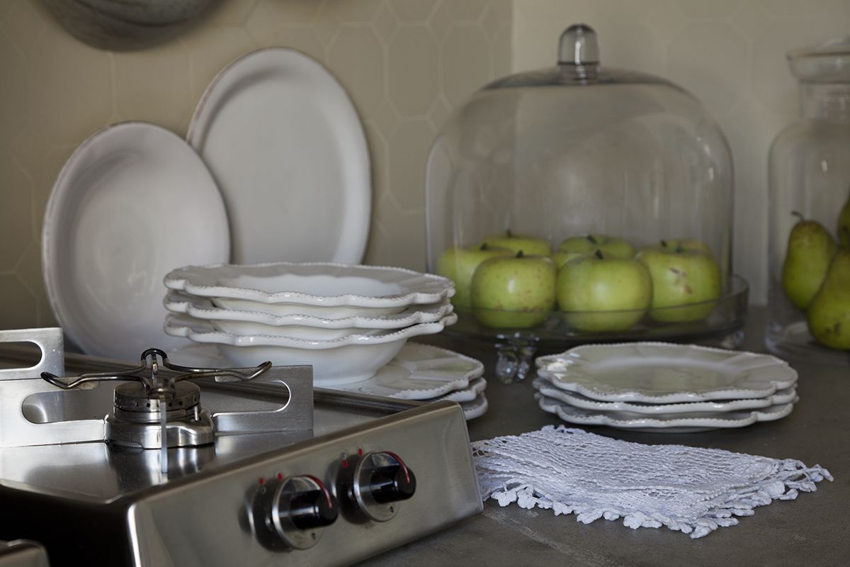 Un comptoir de cuisine sur lequel sont empilées des assiettes blanches, une cuisinière à gaz et un présentoir en verre contenant des pommes vertes.