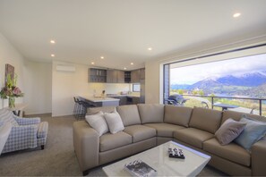 Relax in this serene space with a panoramic mountain view, featuring a comfortable sofa and a well-equipped kitchen.