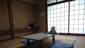 A tatami mat room with a low table, cushions, a kettle, and a small shelf with items. - Hotel Shirahama (Shirahama)