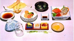 A table with various Japanese dishes, including sushi, sashimi, and tempura, along with small bowls of soy sauce and pickled ginger. - Hotel Shirahama (Shirahama)