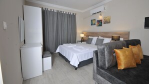Una habitación de hotel con cama, sofá, escritorio y ventana con cortinas.