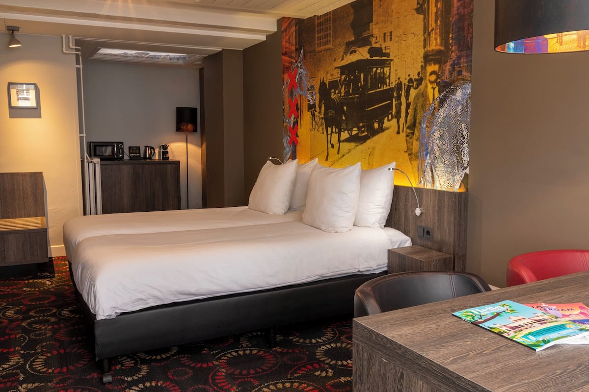 Habitación de hotel con una cama grande, un escritorio, una silla roja, un microondas, una cafetera y un mural grande en la pared.