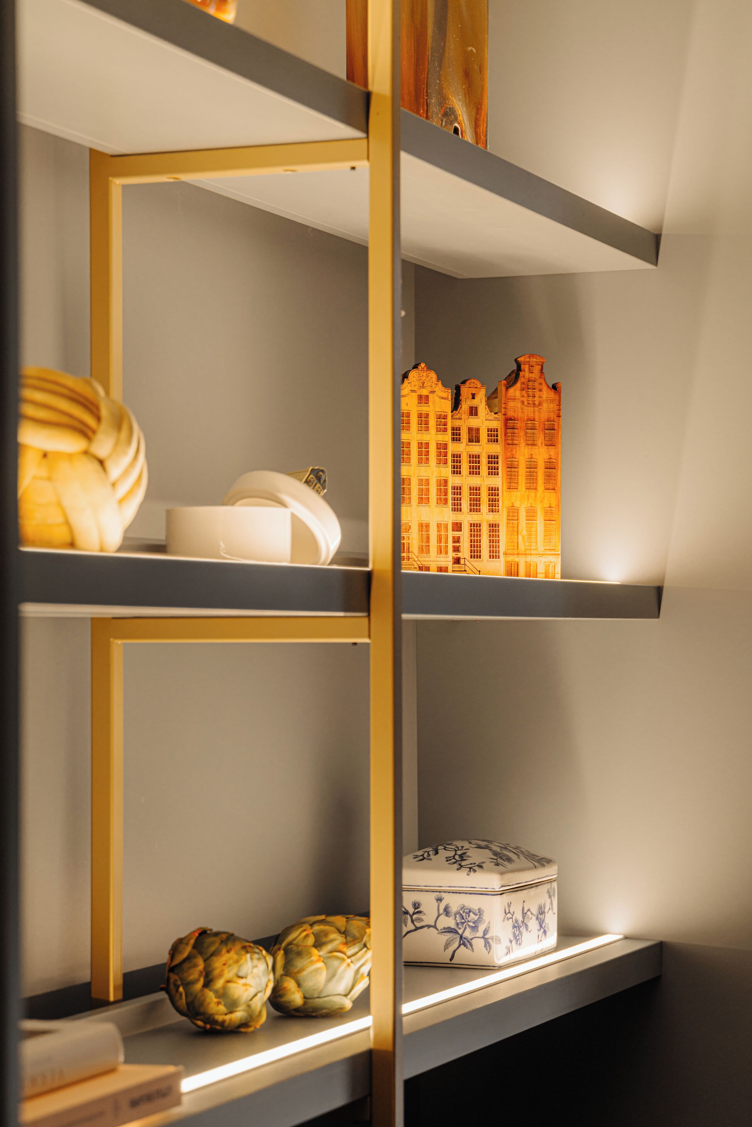 A shelf with decorative items including a model of a building, a white vase, and two artichokes.