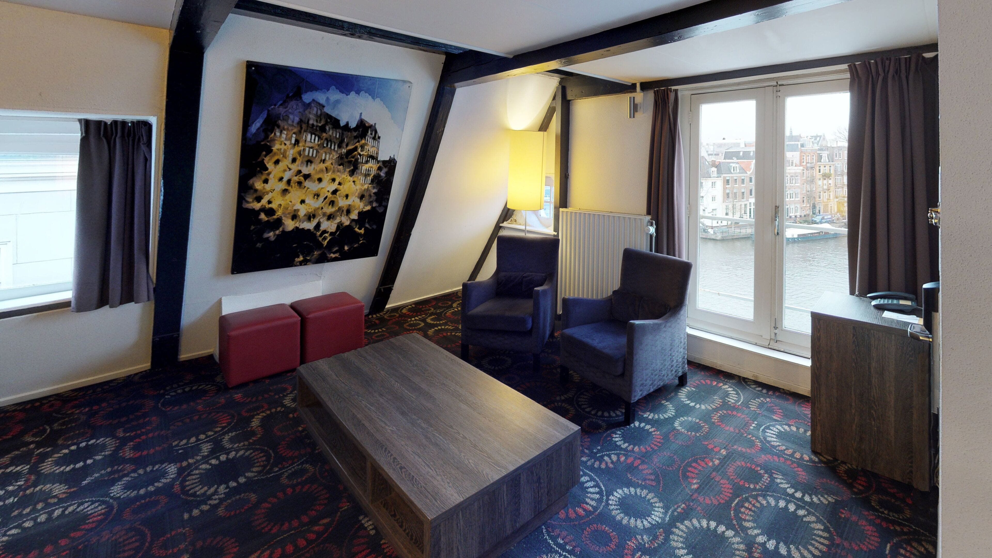 Ein Hotelzimmer mit großem Fenster, einem Gemälde, einer Couch, einem Sessel und einem Holztisch.