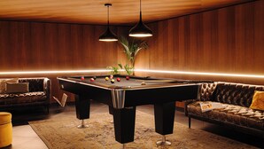 A pool table in a room with wooden walls, a sofa, and two pendant lights. - Leonardo Eden Hotel Amsterdam City Center (Amsterdam)