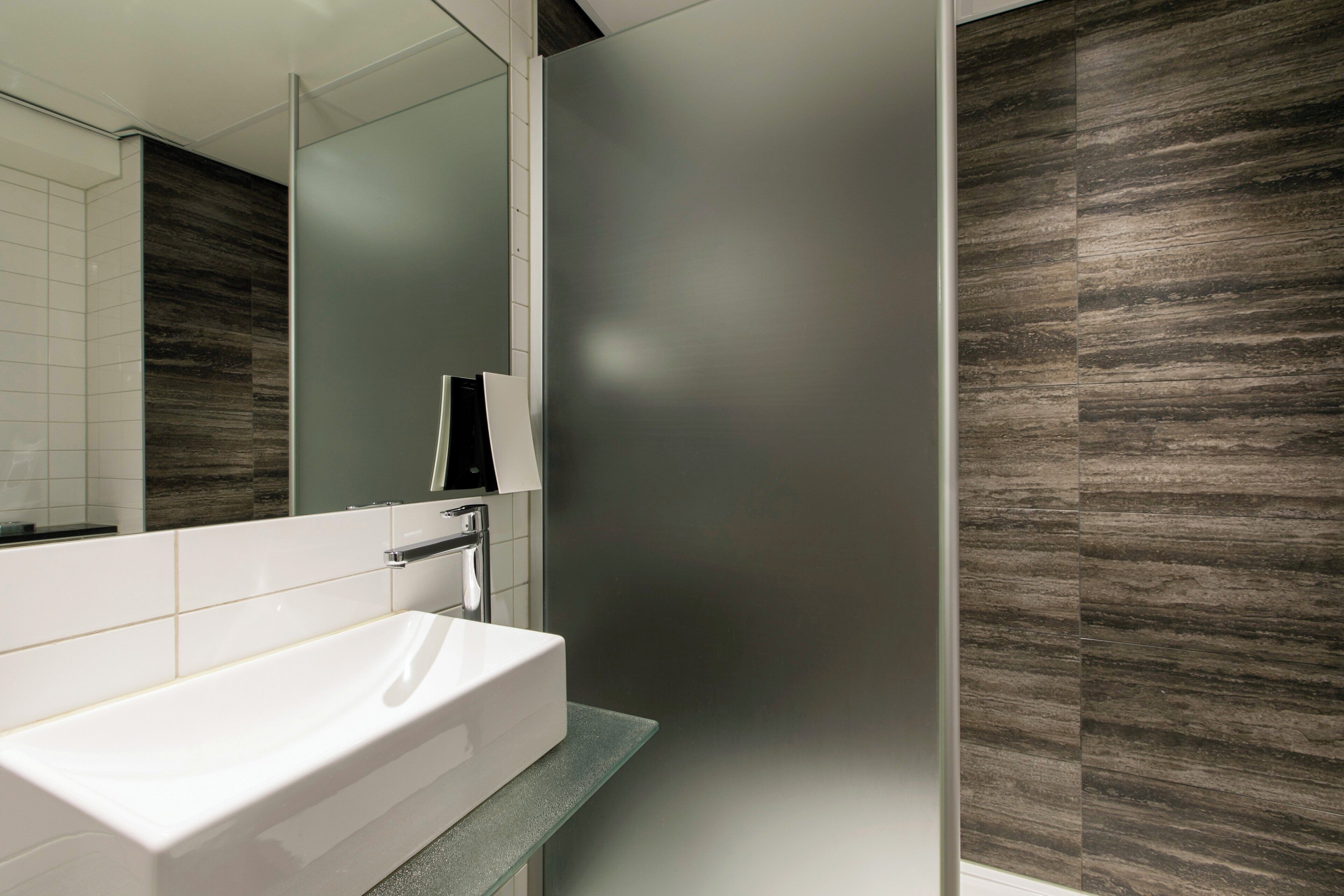 A modern bathroom with a white sink, a mirror, and a shower area.