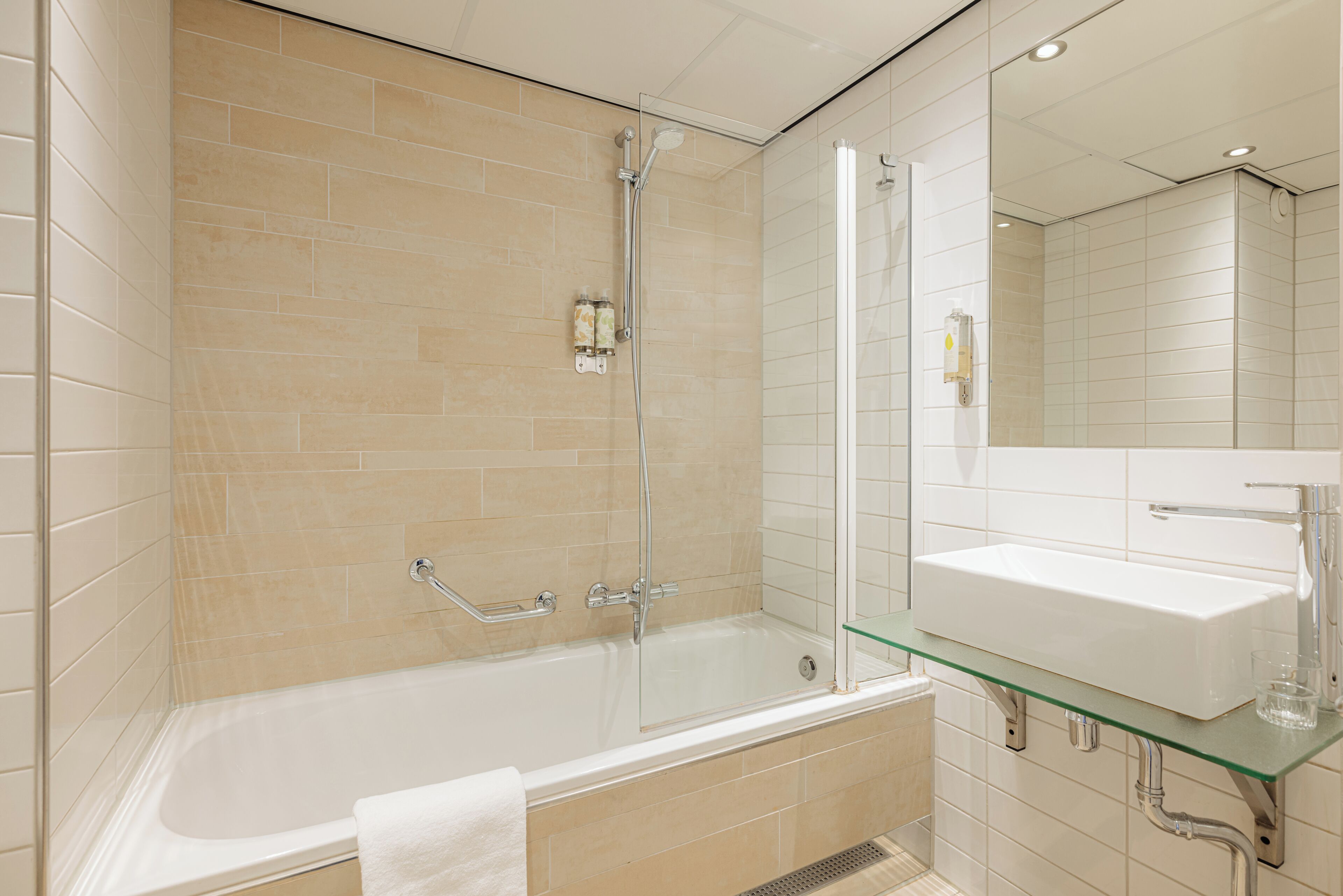 A modern bathroom with a glass-enclosed shower, a glass-topped sink, and a white bathtub.