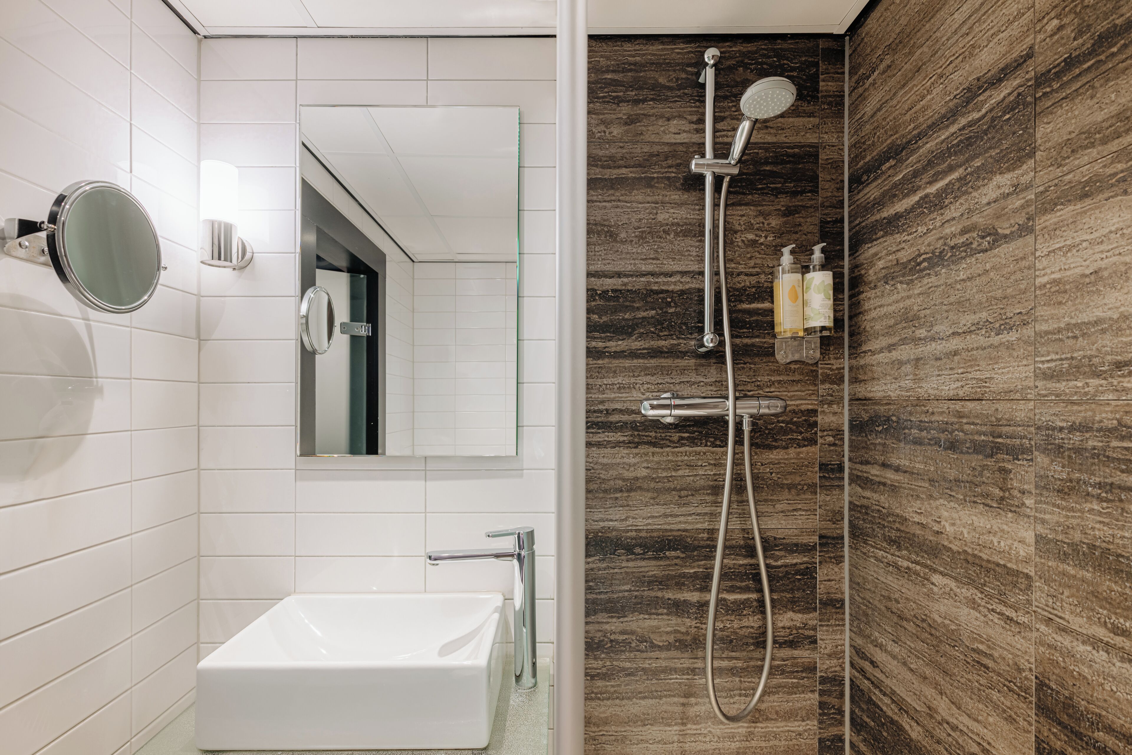 A modern bathroom with a white sink, a mirror, and a shower with a wooden wall.