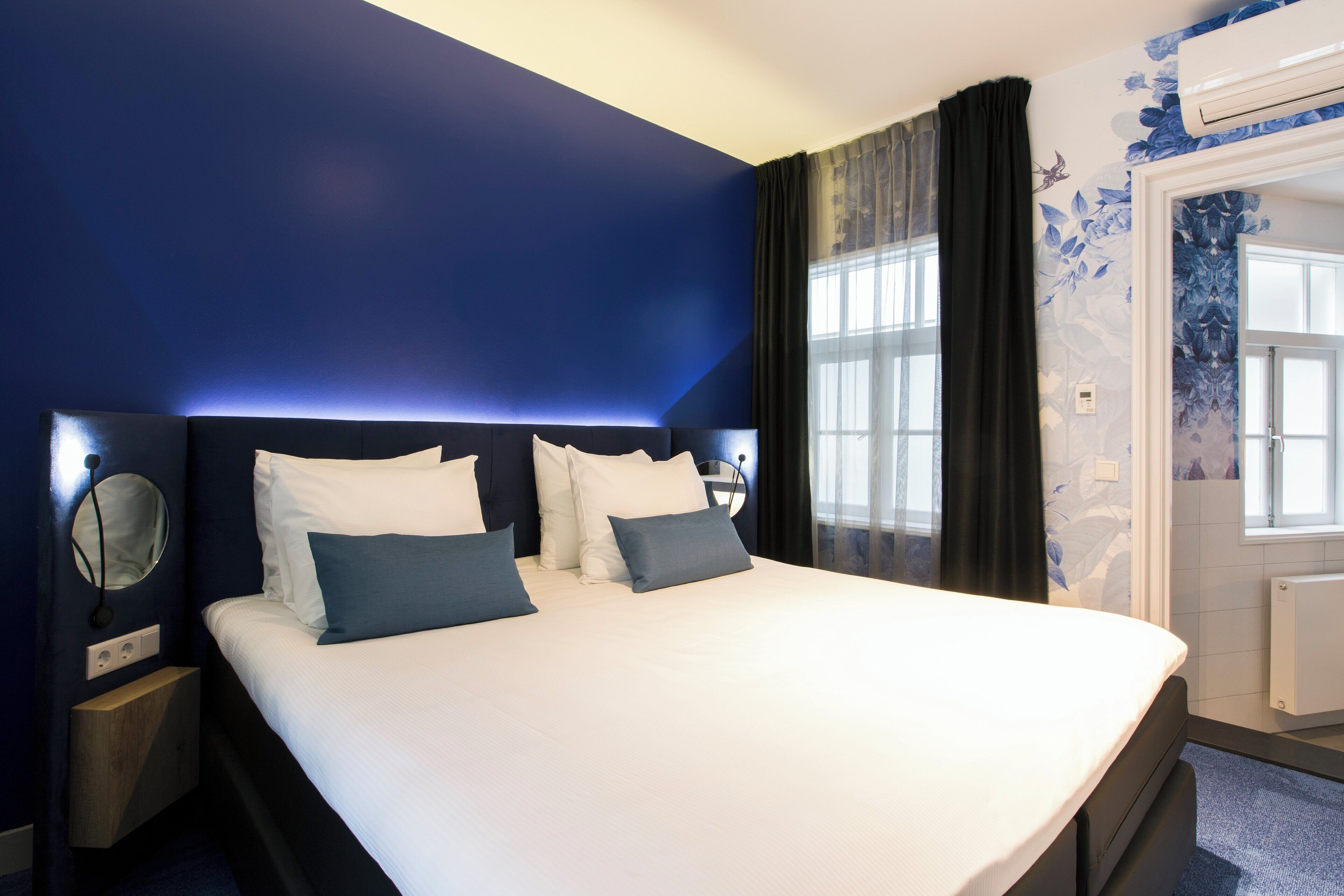 A hotel room with a large bed, dark blue walls, and a window with curtains.