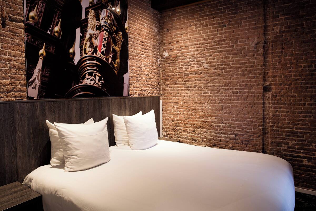 Una cama bien hecha con sábanas y almohadas blancas, una pared de ladrillo y un cabecero de madera.