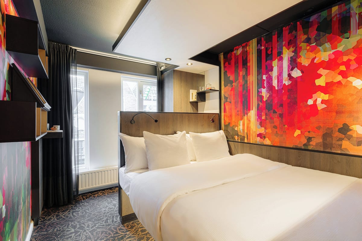 Habitación de hotel con una cama grande, una ventana con cortinas, un muro decorativo abstracto y un estante empotrado.