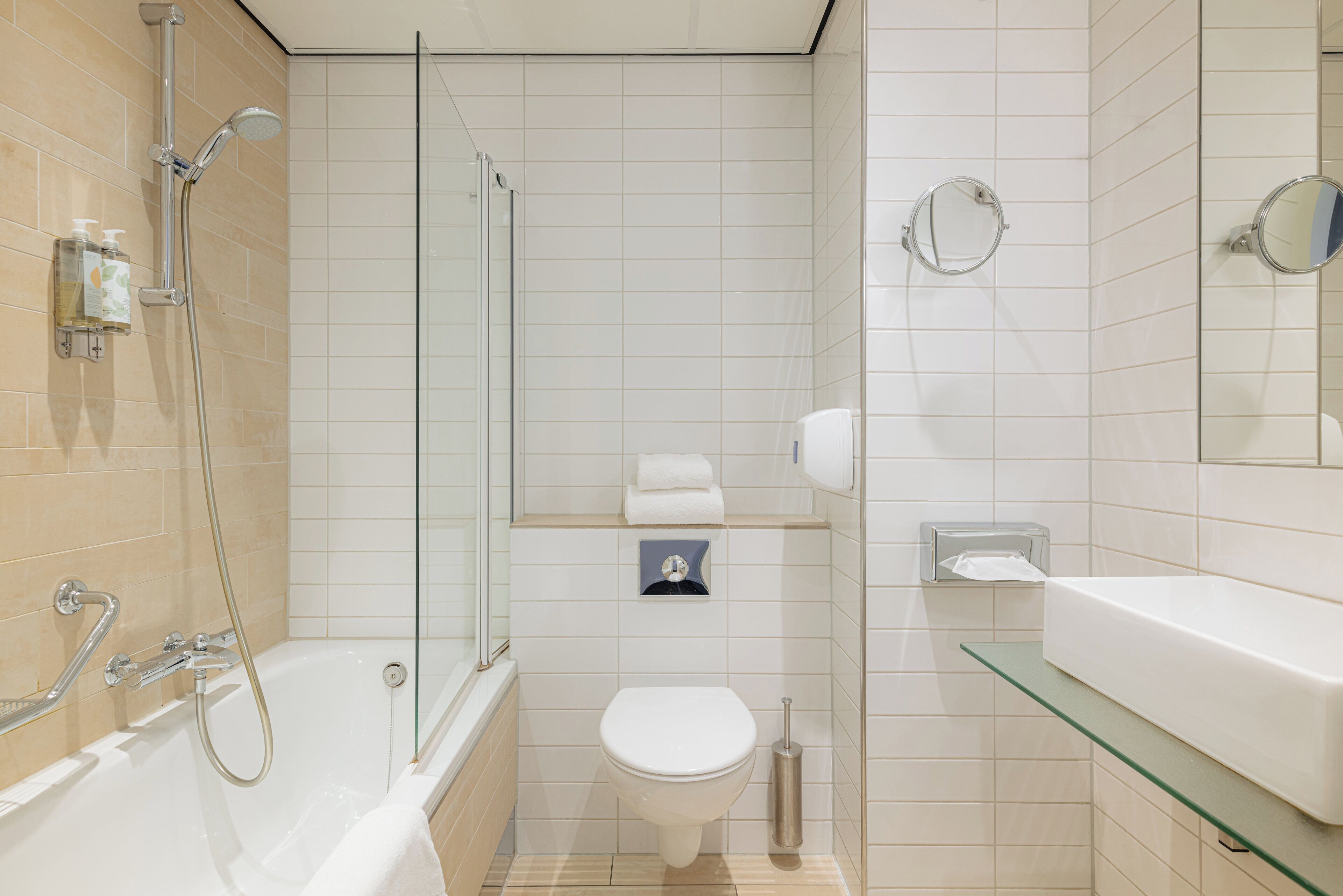 A modern bathroom with a glass-enclosed shower, a white toilet, and a glass shelf above the sink.