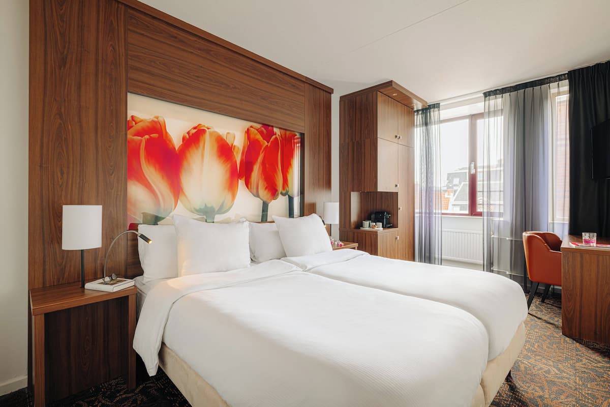 Una habitación de hotel con una cama grande, un escritorio, una silla y un ventanal con cortinas.