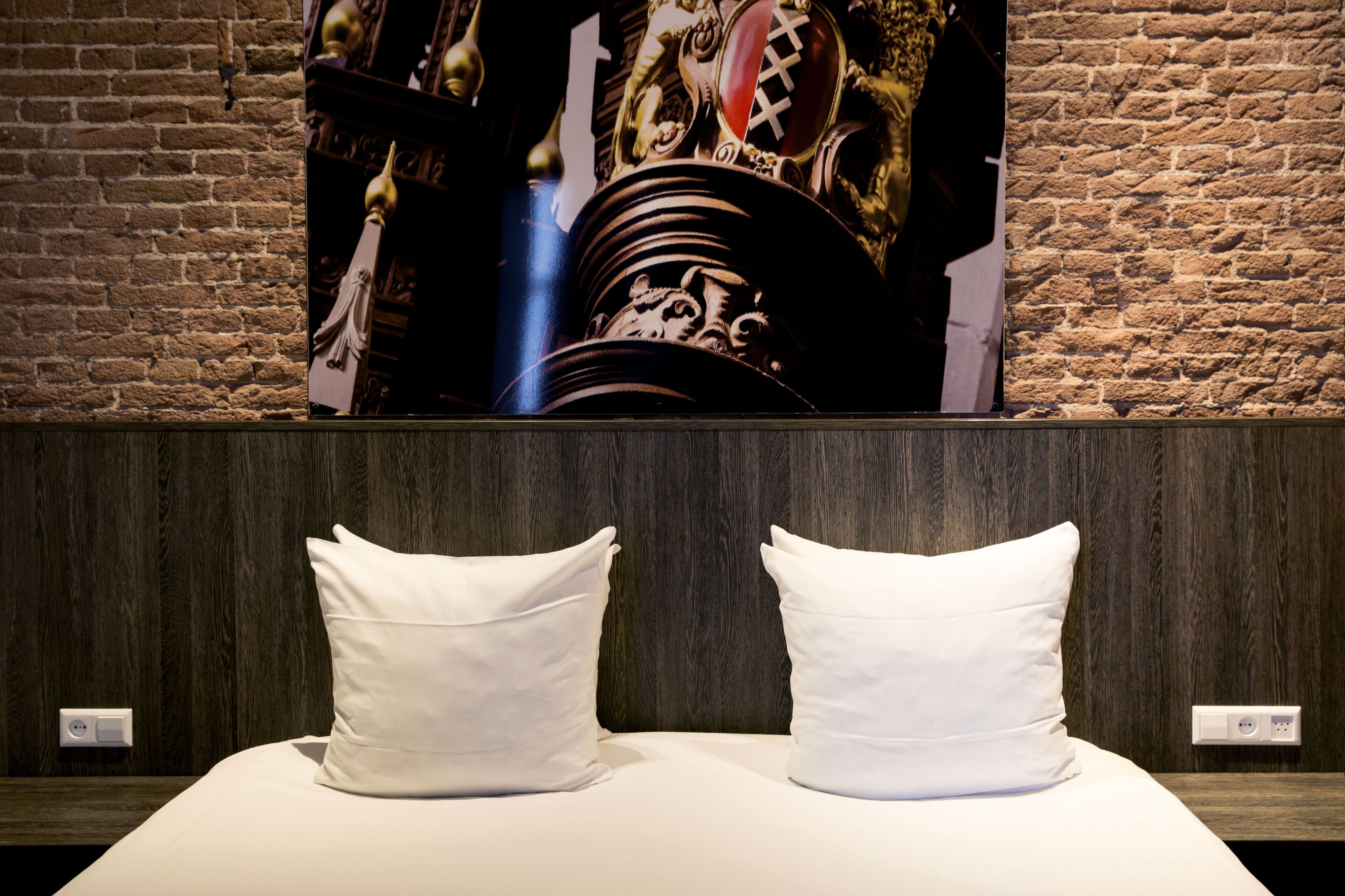Una habitación de hotel con cabecera de madera, cama con ropa de cama blanca y un cuadro decorativo grande sobre la cama.