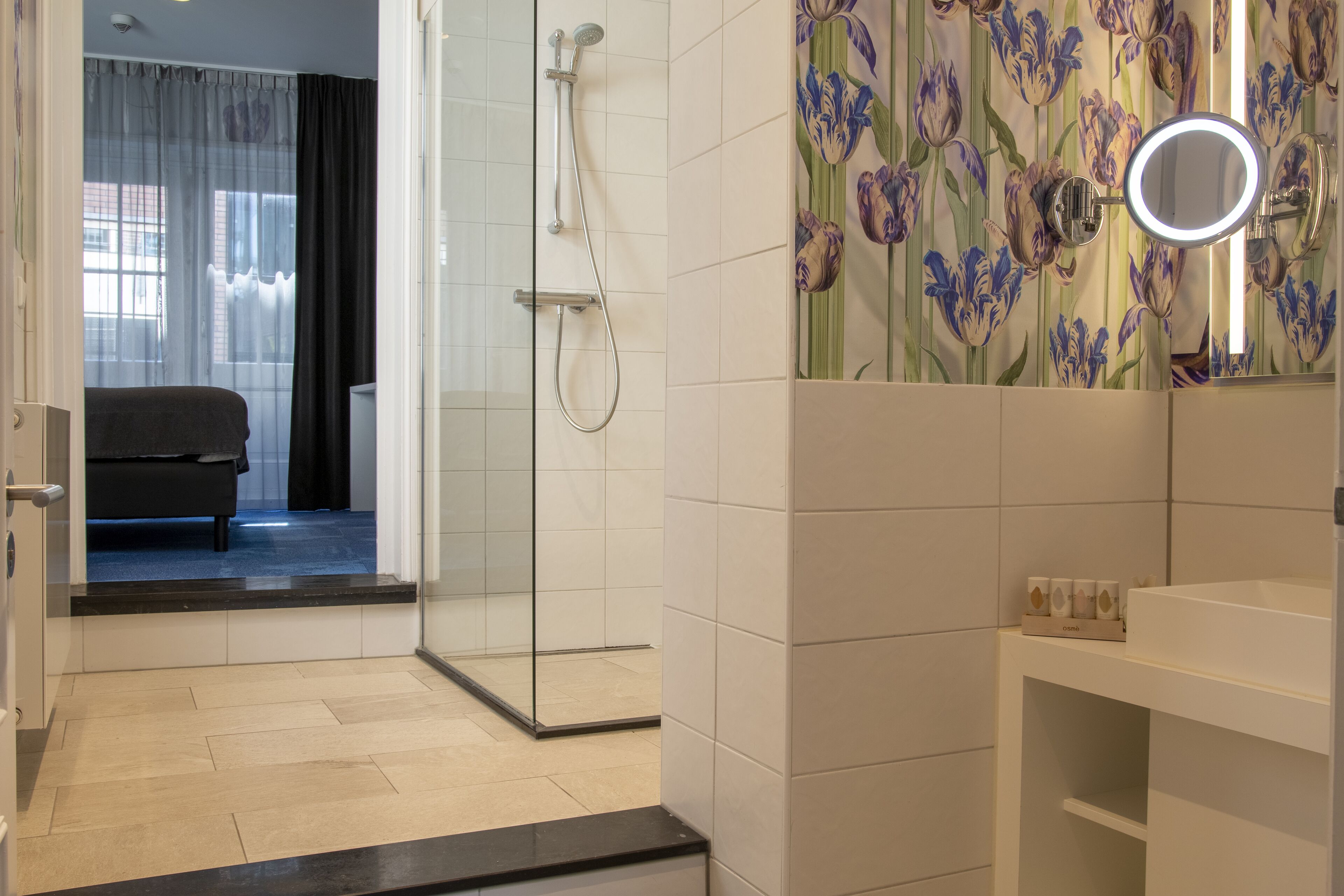 A modern bathroom with a glass shower enclosure, a vanity with a mirror, and a floral wallpaper design.