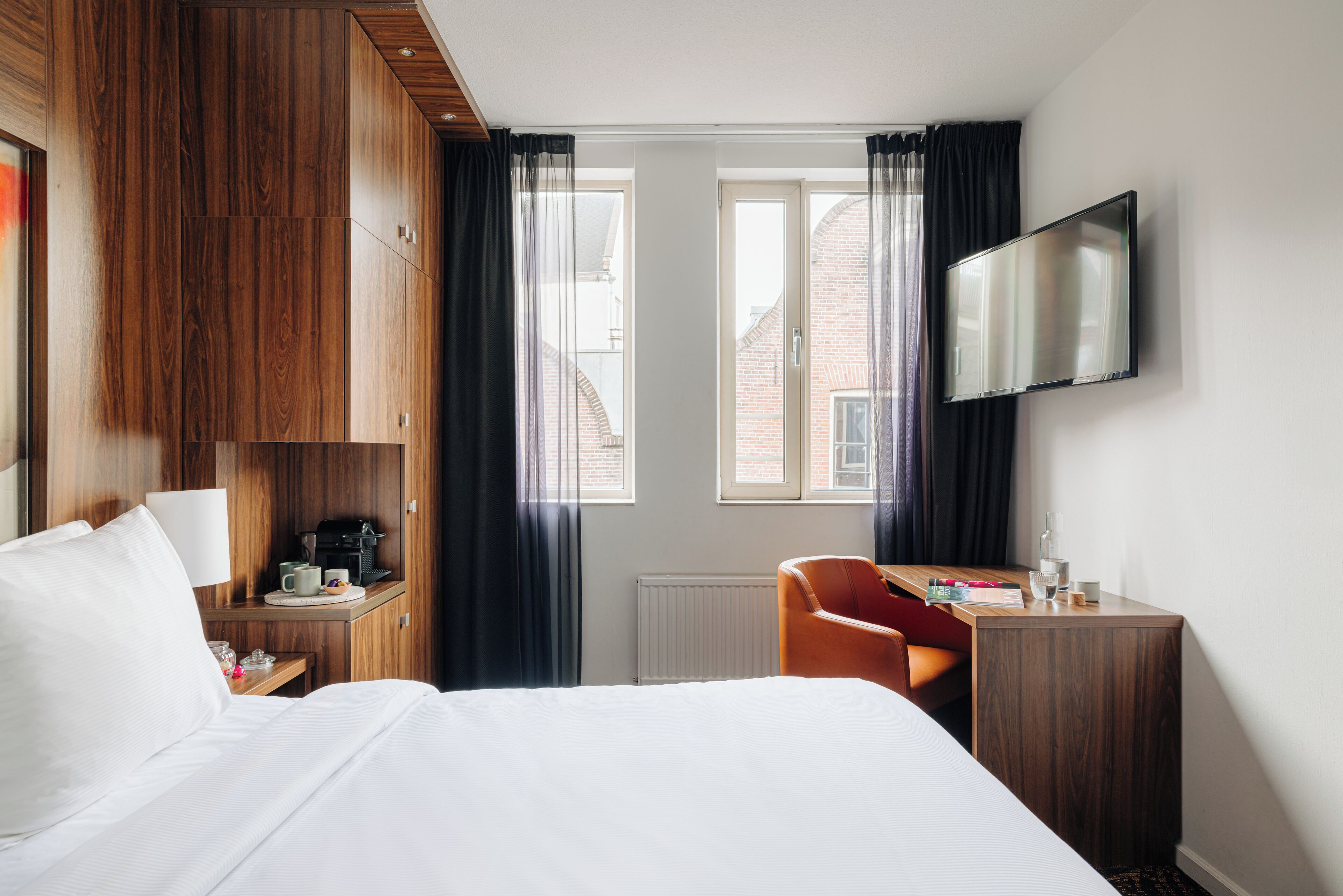 A hotel room with a bed, a desk with a chair, a television, and a window with curtains.