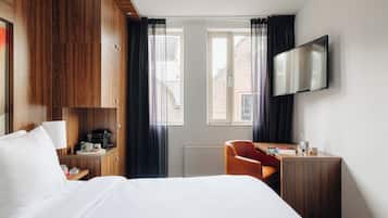 Habitación de hotel con cama, escritorio, silla, televisión y ventana con cortinas.