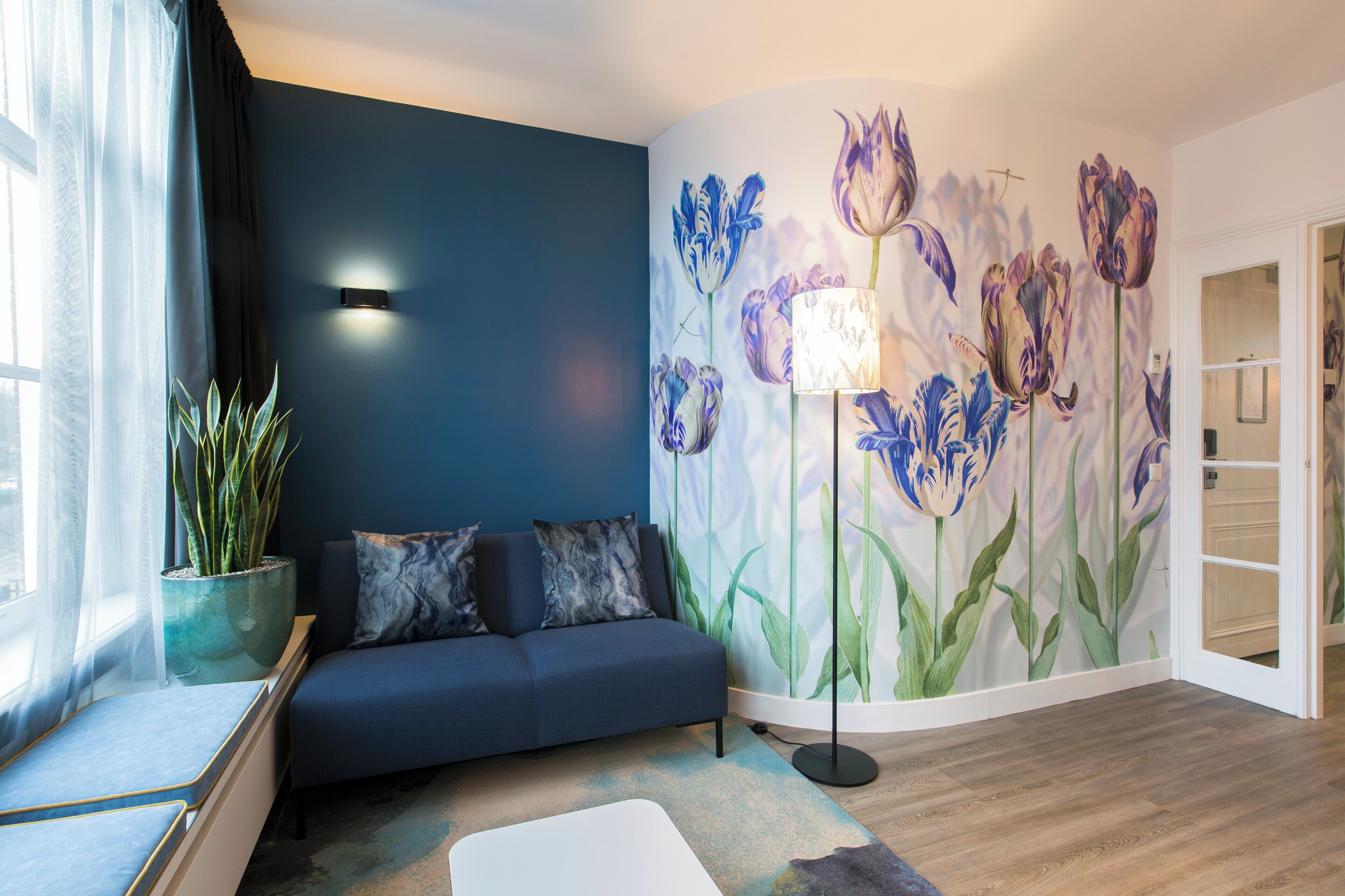 A modern living room with a dark blue sofa, a floor lamp, and a wall mural of flowers.