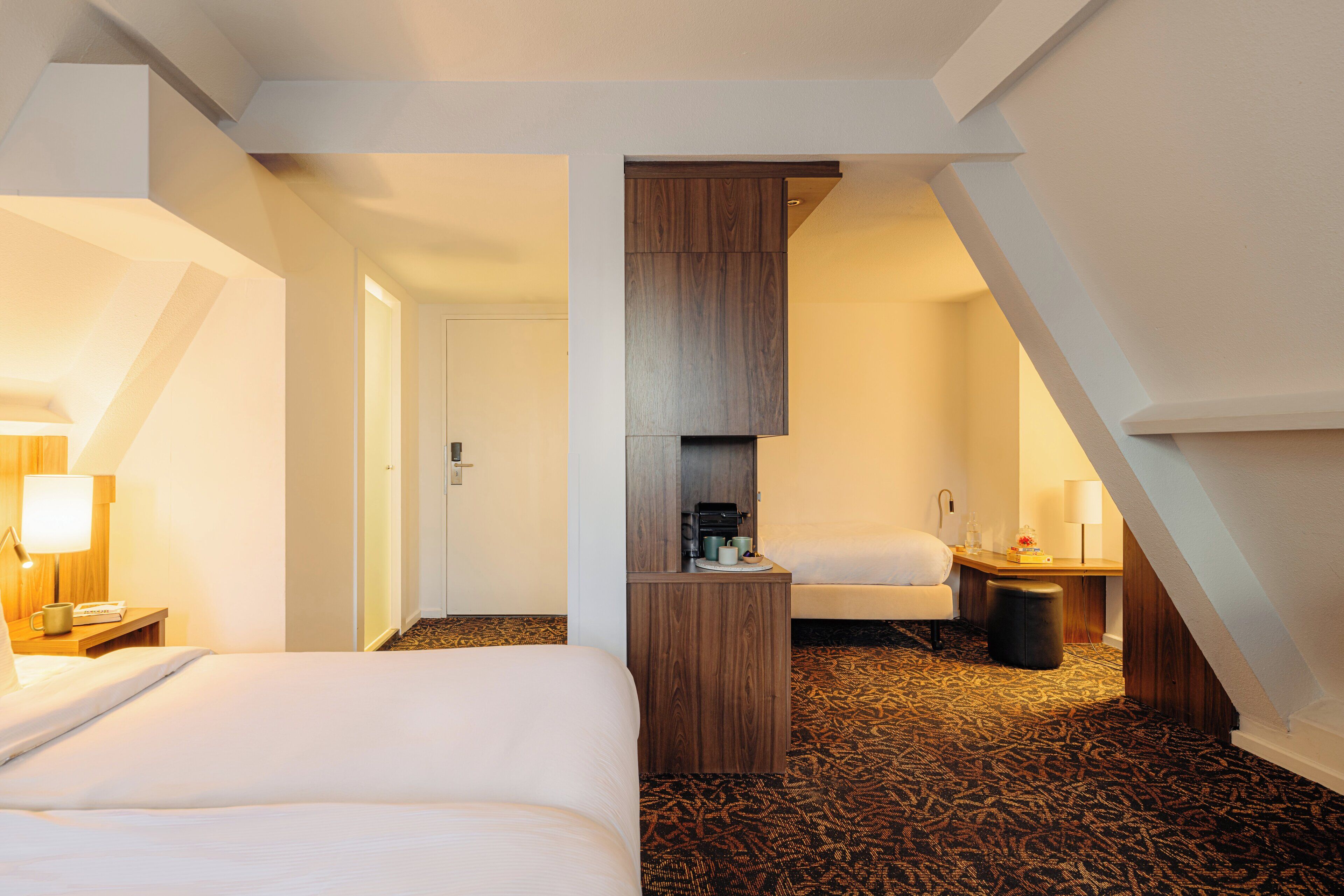 Hotellihuone, jossa on suuri sänky, puinen kaappi, pieni pöytä lampun kanssa ja kuviollinen matto.