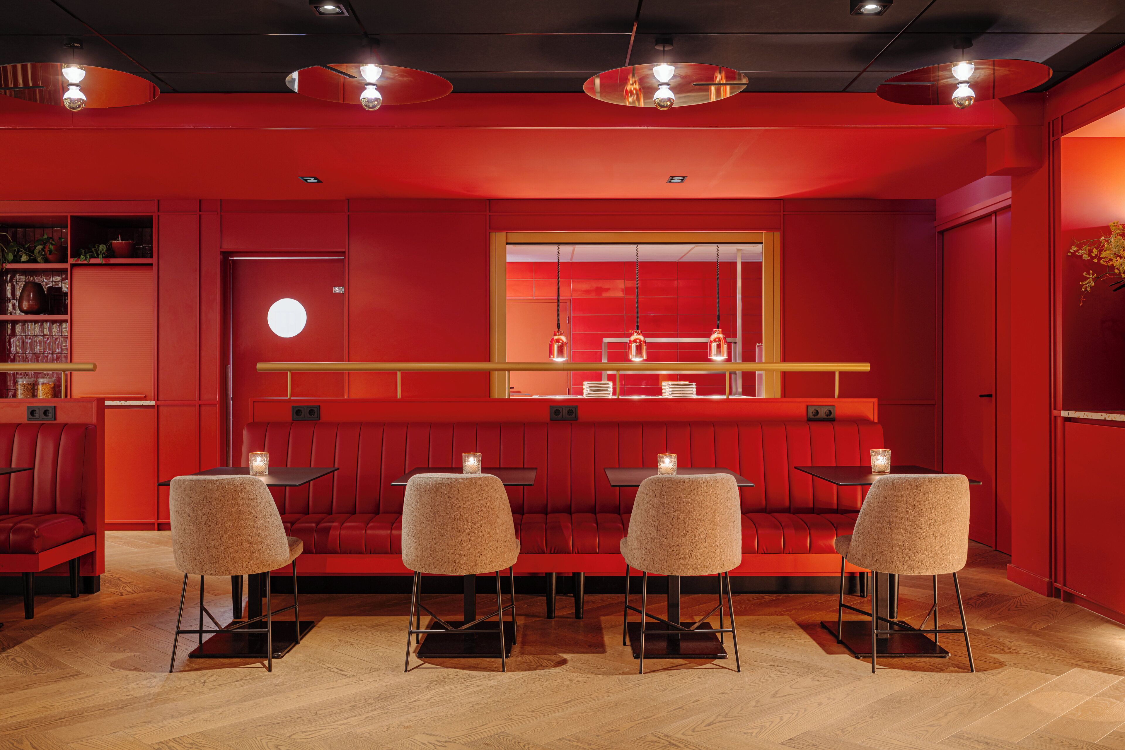 A red-themed restaurant with booth seating, pendant lighting, and a large mirror.