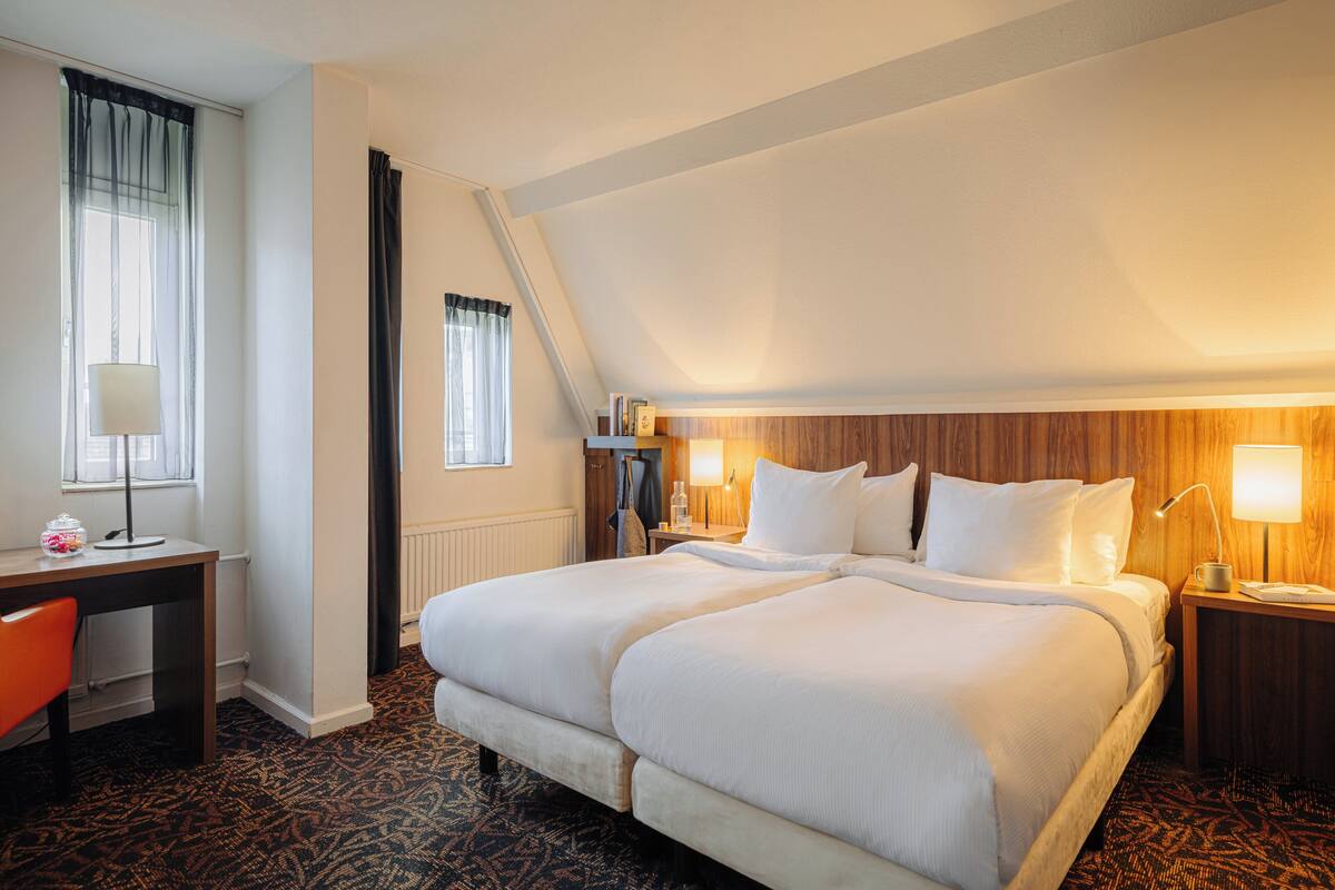 Una habitación de hotel con una cama grande, un escritorio, una silla, una lámpara y una ventana con cortinas.