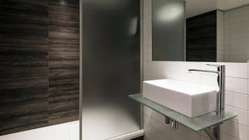 Ein modernes Badezimmer mit Ablagefläche aus Glas, auf der ein weißes Waschbecken steht, einem Spiegel darüber und dunklen Holzpaneelen an den Wänden.