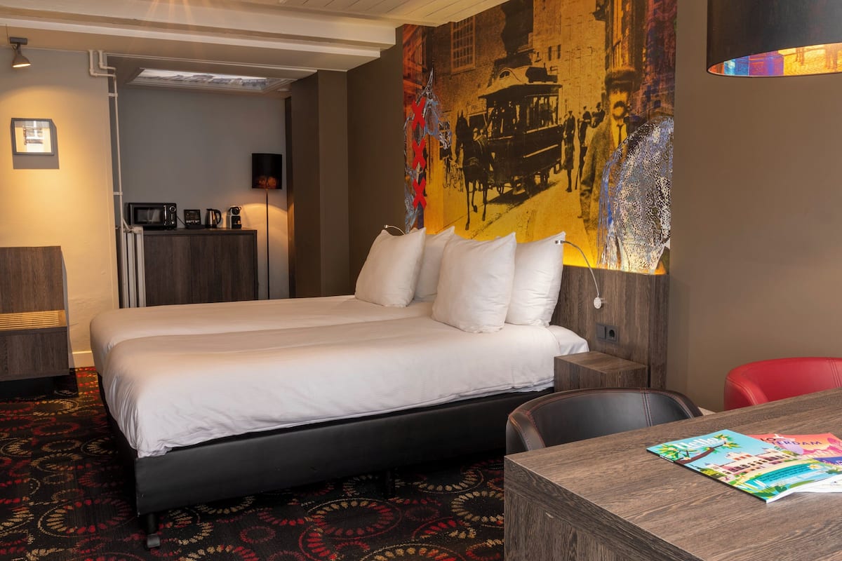 A hotel room with a large bed, a desk, a red chair, a microwave, a coffee maker, and a large wall mural.