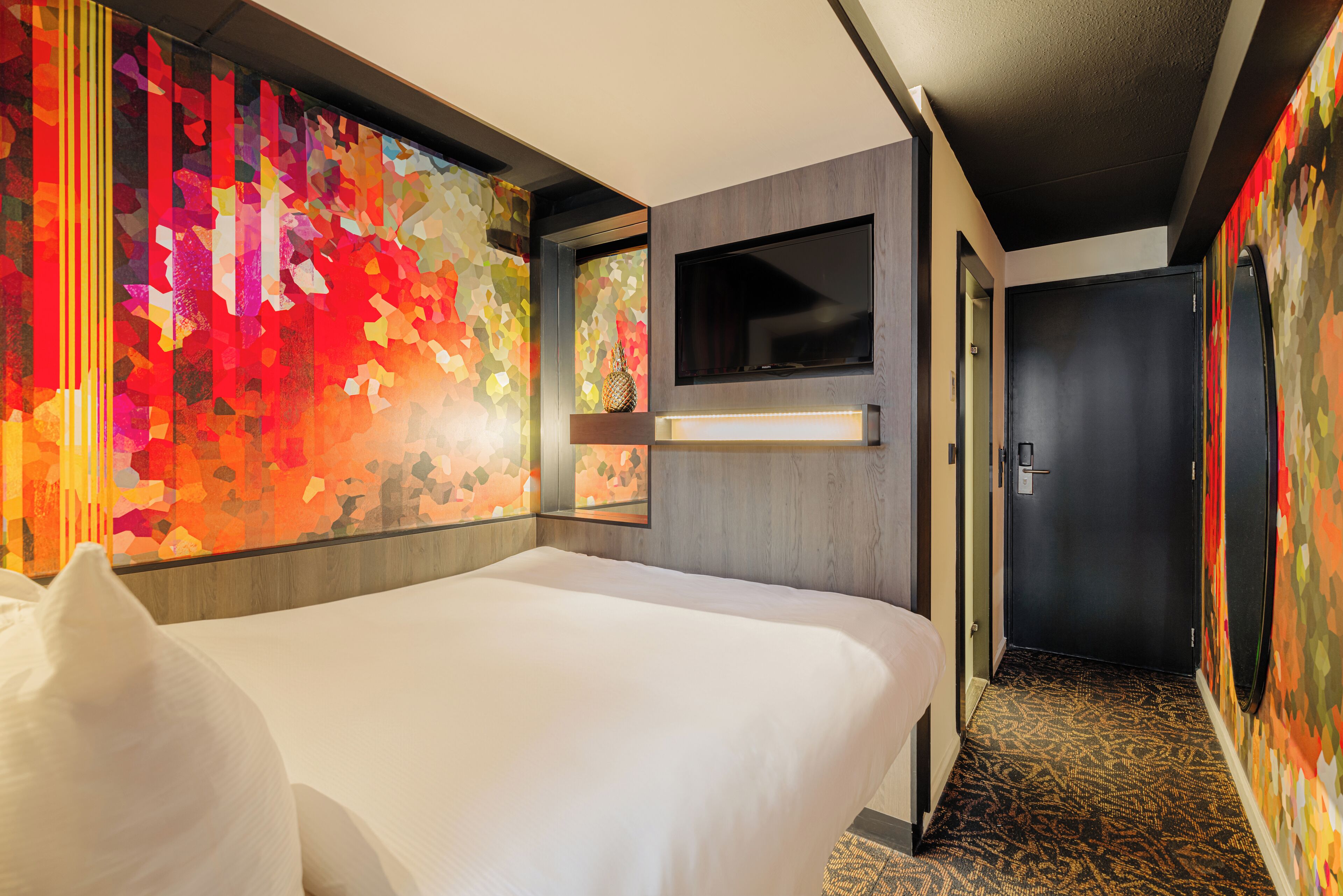 A hotel room with a large bed, a TV mounted on the wall, and a colorful abstract wall art.