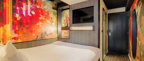 A hotel room with a large bed, a TV mounted on the wall, and a colorful abstract wall art.