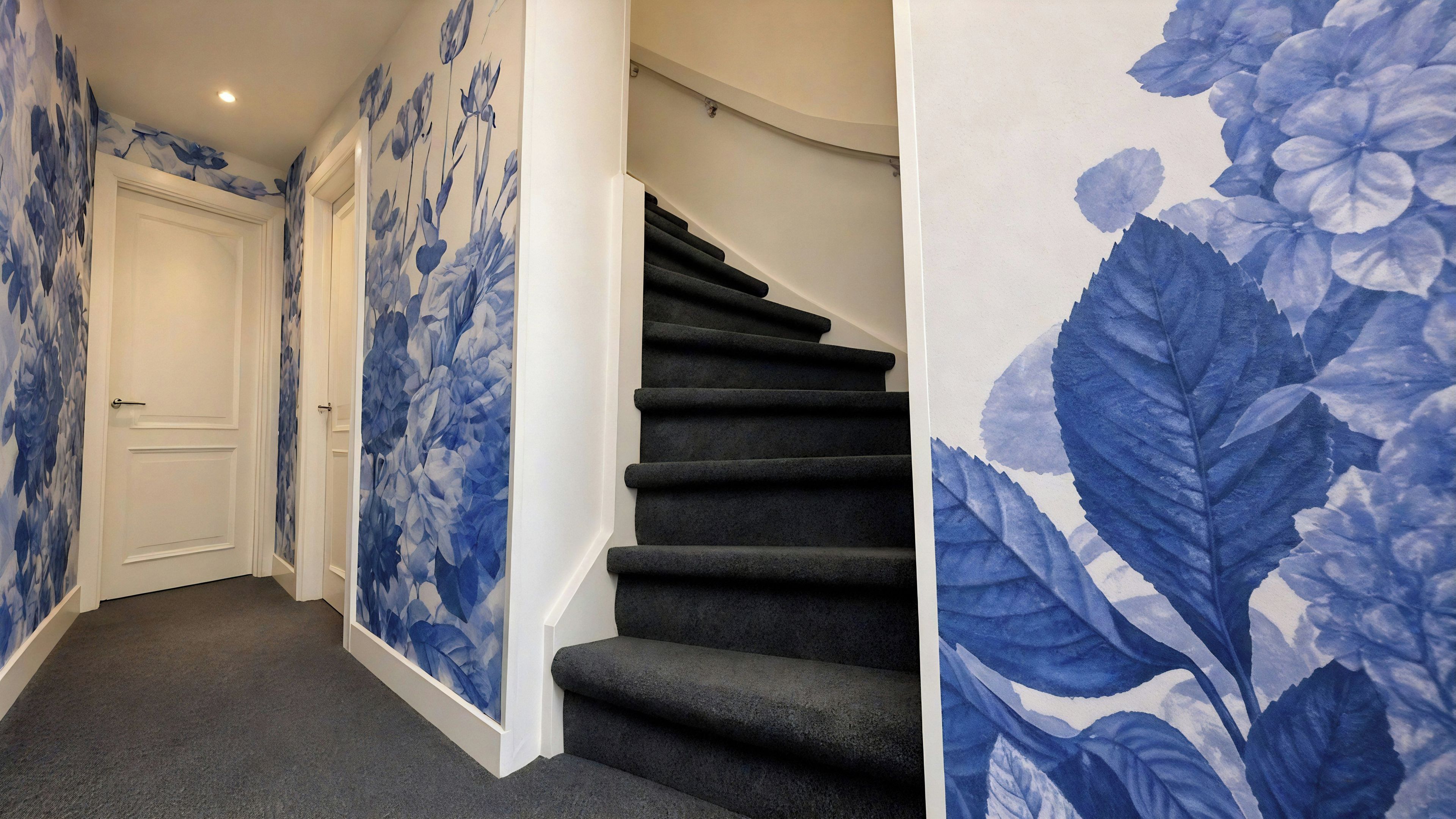 A hallway with a carpeted floor, a white door, and a staircase with a dark carpet.