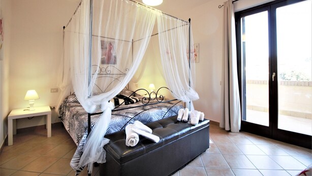 A bedroom with a four-poster bed, a bedside table with a lamp, and a large window with a view.