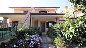 A two-story house with a front entrance, a small garden with flowers, and a metal fence.