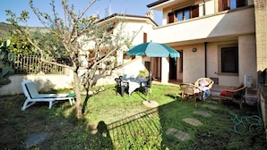 A courtyard with a table and chairs under a blue umbrella, surrounded by a garden and a building with balconies.