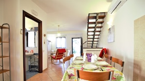 A dining area with a table set for four, a staircase, and a view of the adjacent room.