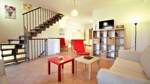 A living room with a staircase, a red chair, a white sofa, and a bookshelf.