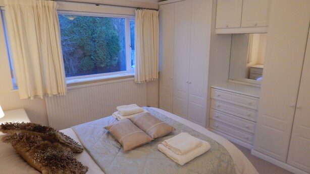 A bedroom with a bed, a window with curtains, a wardrobe, and a mirror. - Cherry Palace 3 BD Parking Spaces groups (Cambridge)