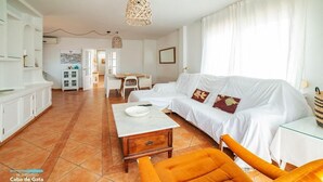 Un amplio salón con sofá blanco, sillón naranja y mesa de comedor.