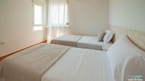 Habitación de hotel con dos camas, una ventana con cortinas traslúcidas y un equipo de aire acondicionado en la pared.
