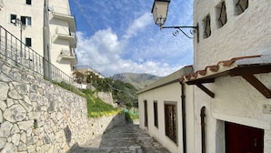 Una estrecha calle empedrada flanqueada por edificios con balcones y una montaña al fondo.