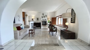 Un amplio salón con sofá, sillones, televisor y chimenea.
